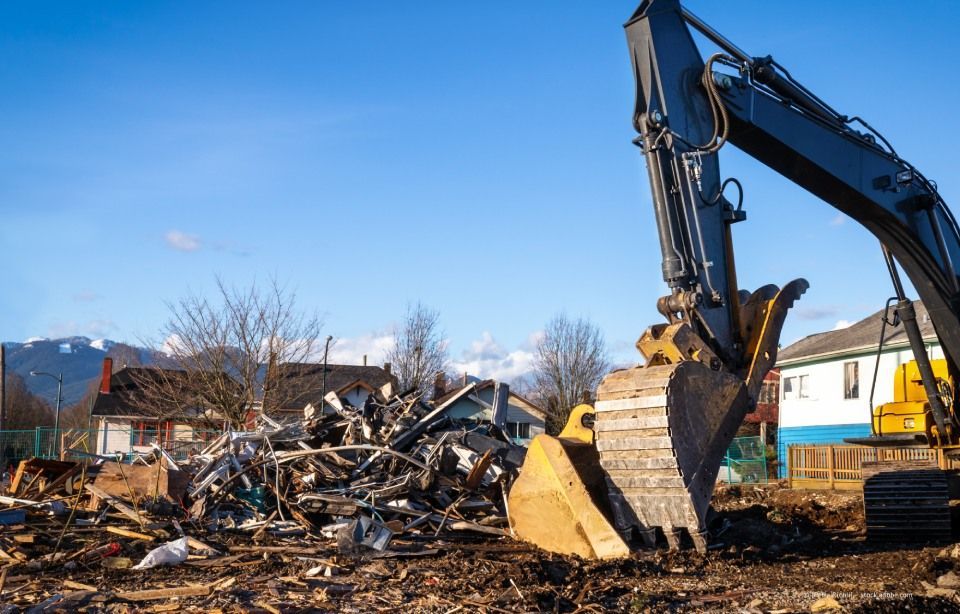 Ein Bagger räumt Bauschutt auf einer Baustelle unter blauem Himmel ab.