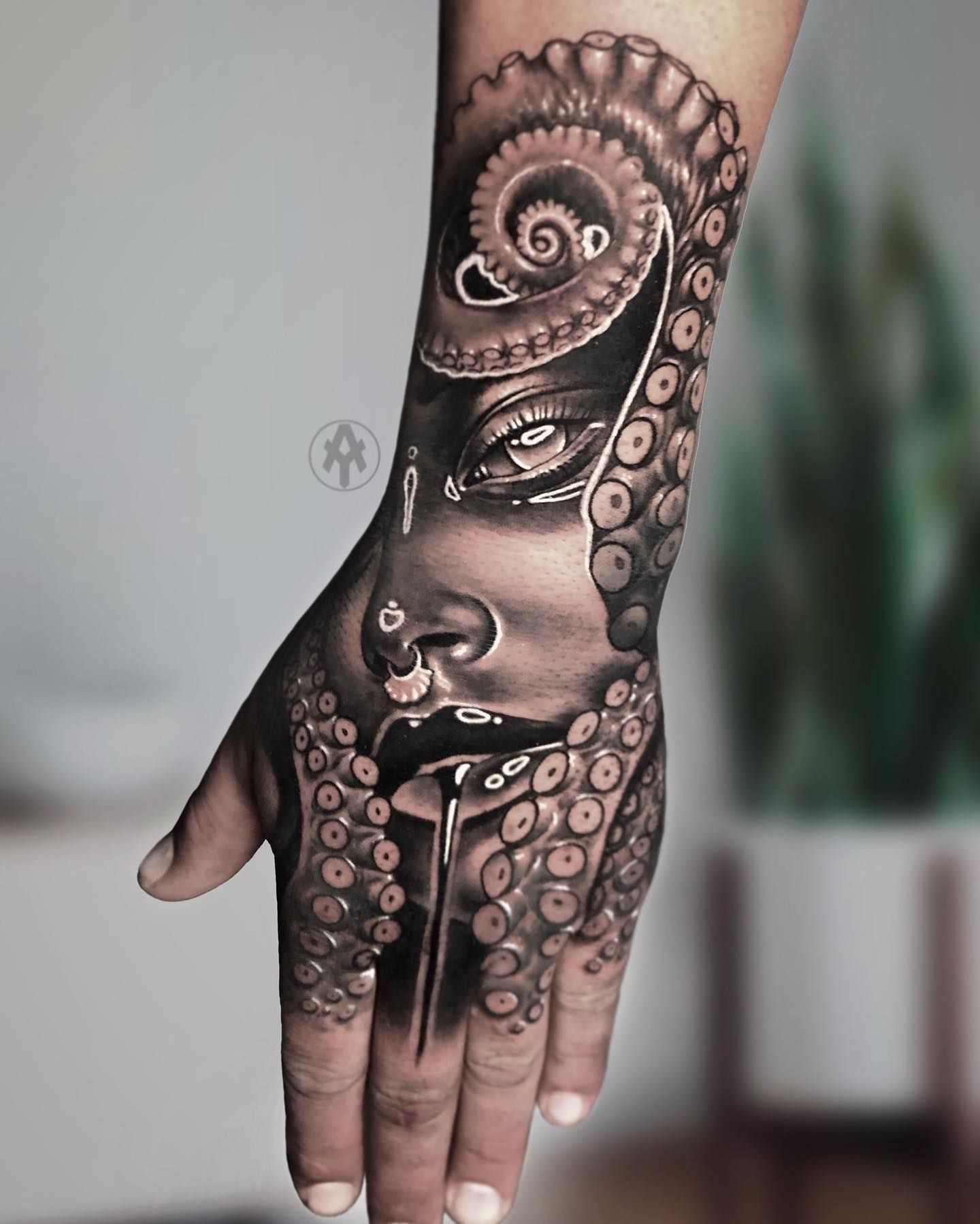 Un primer plano de la mano de una persona con un tatuaje de la cara de una mujer y tentáculos de pulpo.