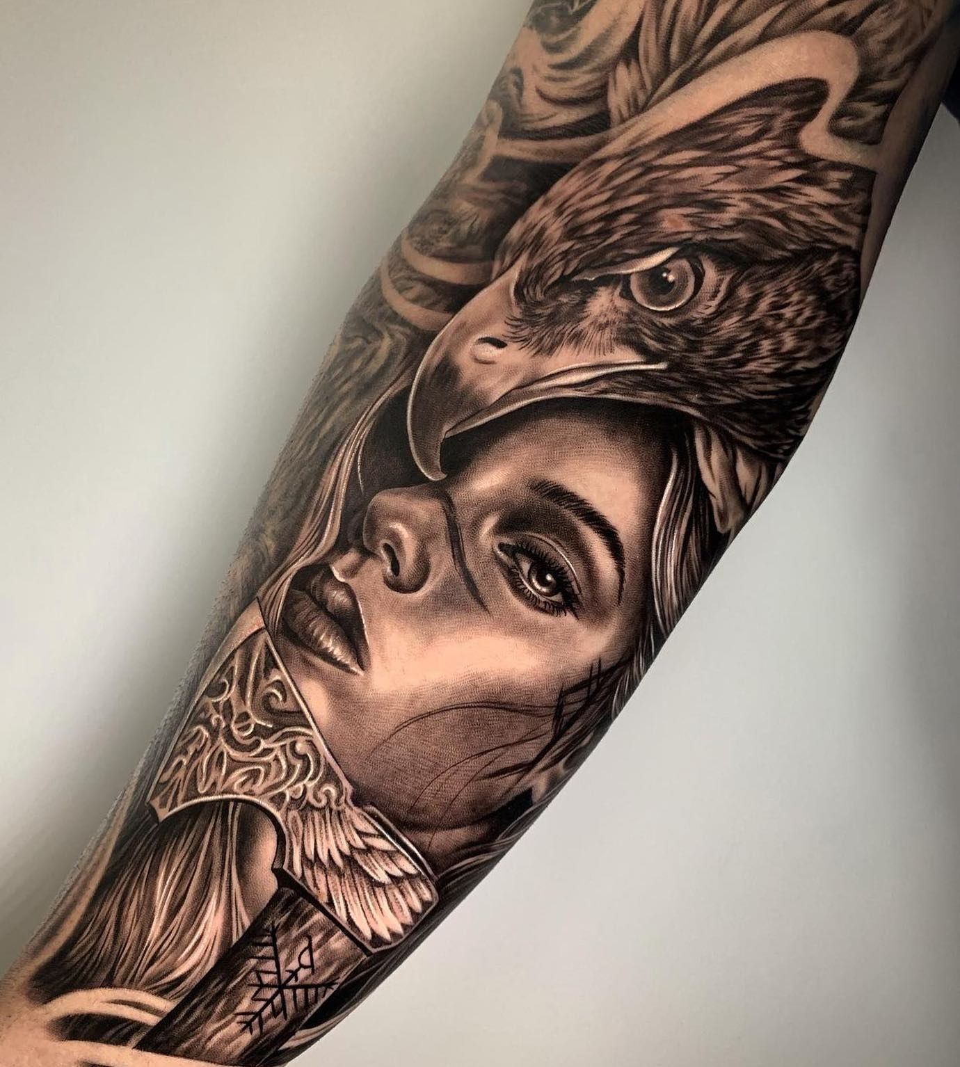 Un tatuaje en blanco y negro de una mujer con un águila en el antebrazo.