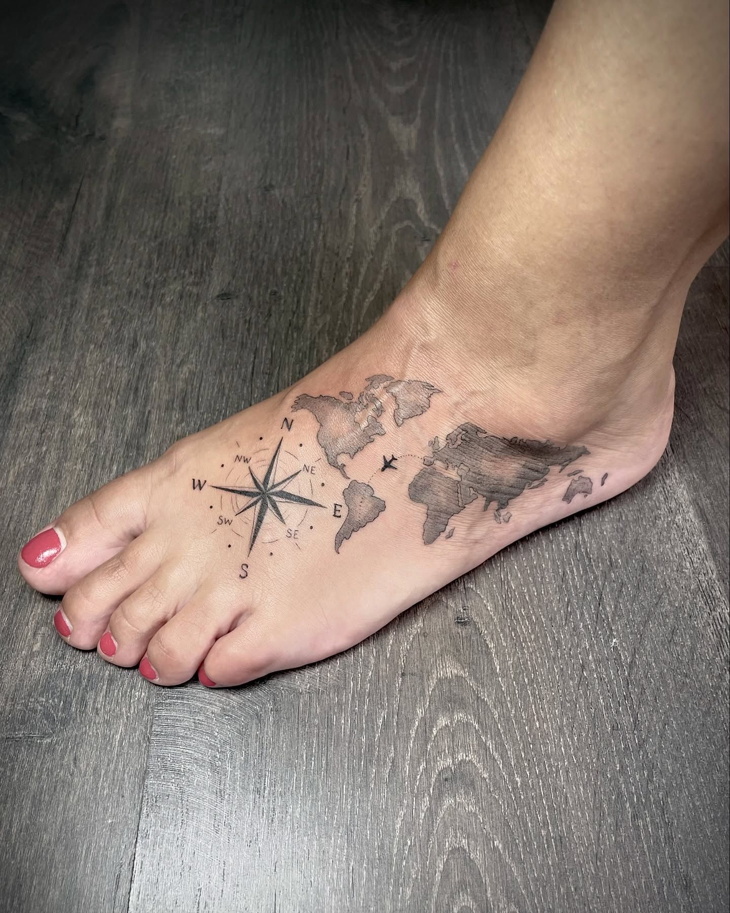 Una mujer tiene un tatuaje de un mapa del mundo y una brújula en el pie.