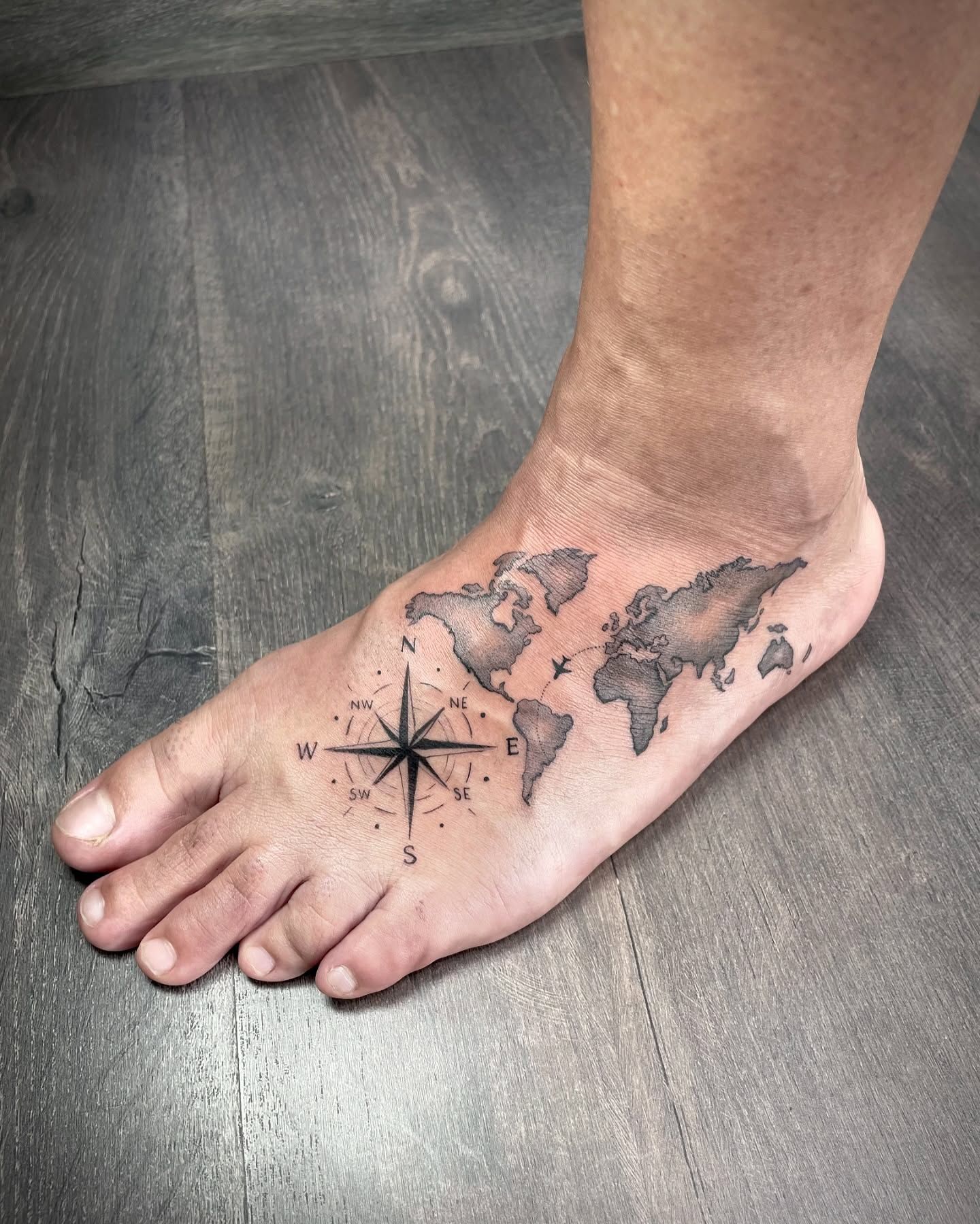 Una persona tiene un tatuaje de un mapa del mundo y una brújula en el pie.