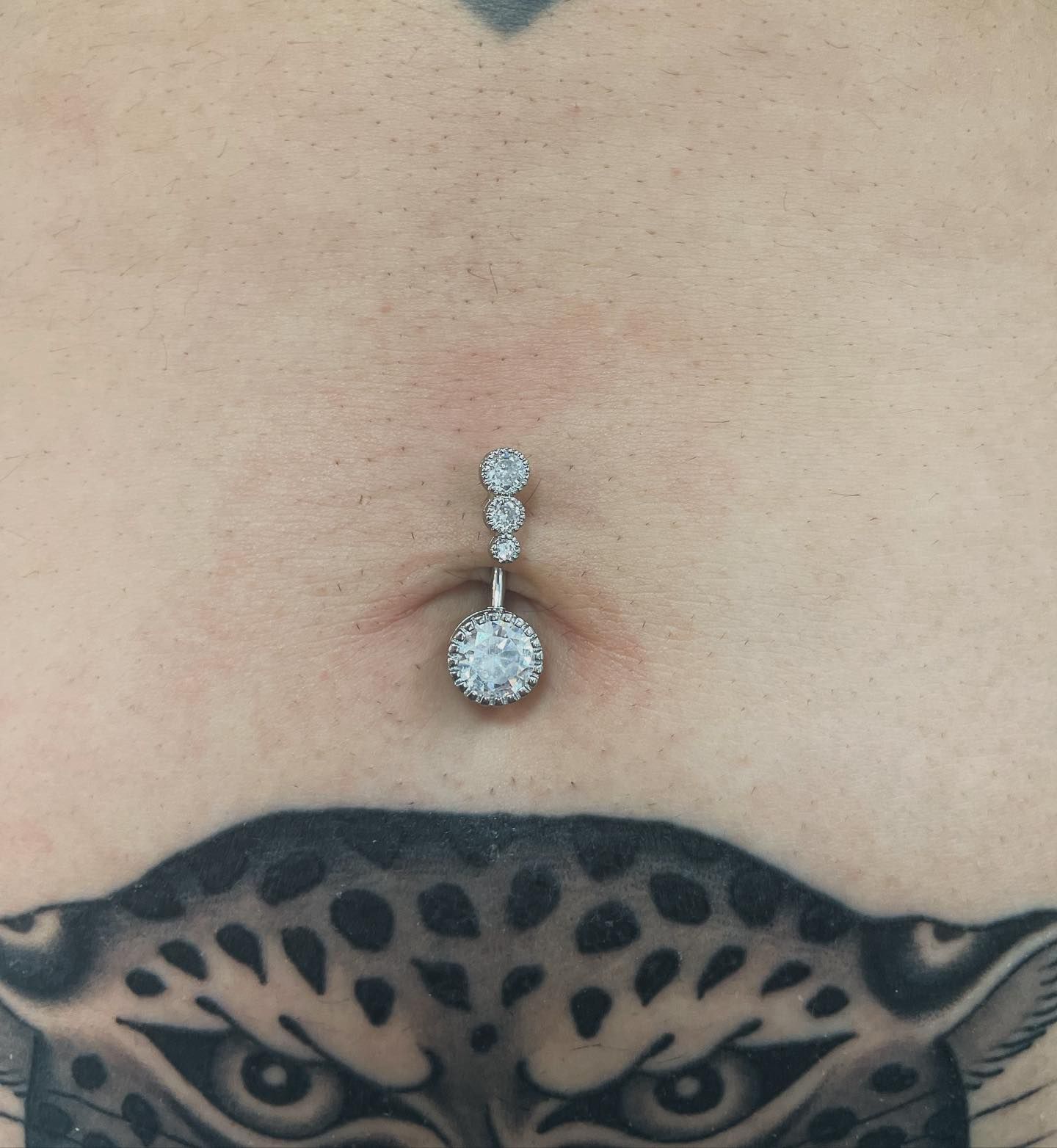 Una persona con un tatuaje de un leopardo en el estómago tiene un piercing en el ombligo.