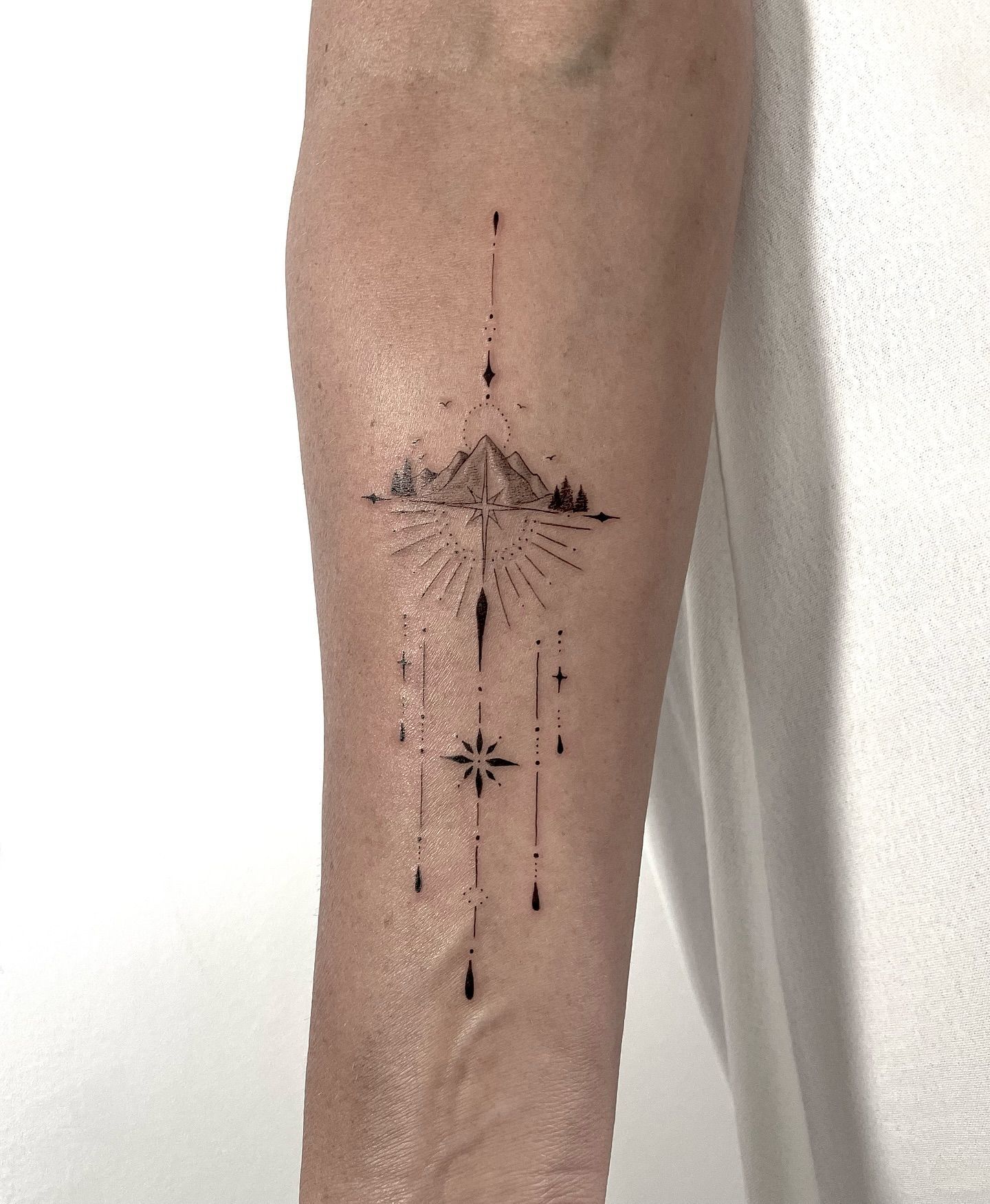 Una persona tiene un tatuaje de una montaña y una estrella en su antebrazo.