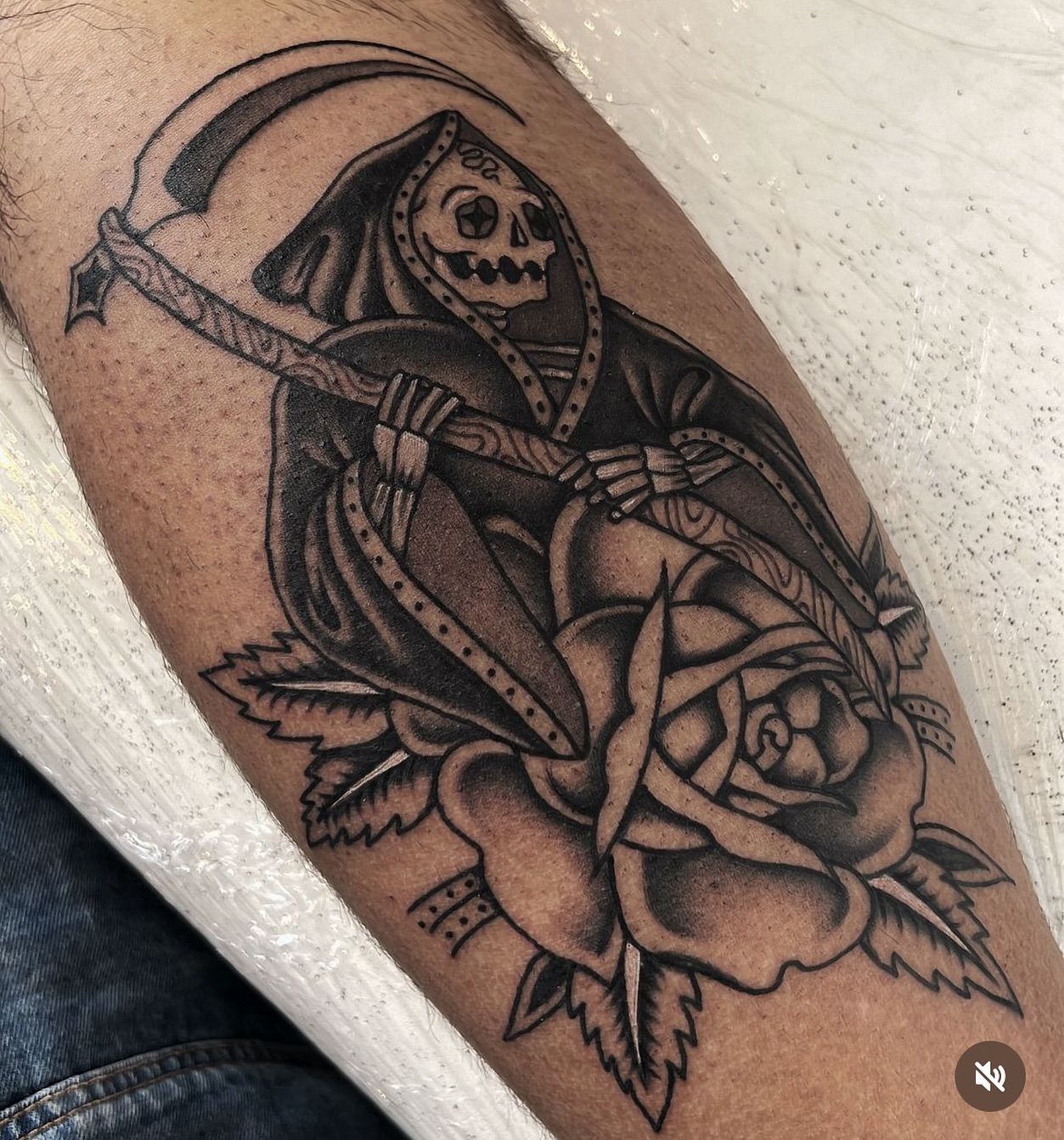 Un tatuaje de una parca sosteniendo una guadaña y una rosa.