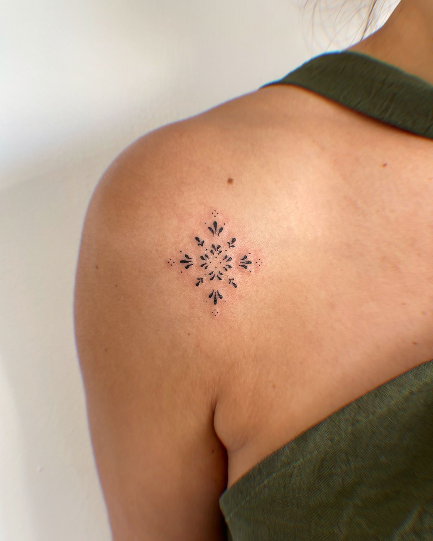 Una mujer tiene un pequeño tatuaje de un copo de nieve en el hombro.