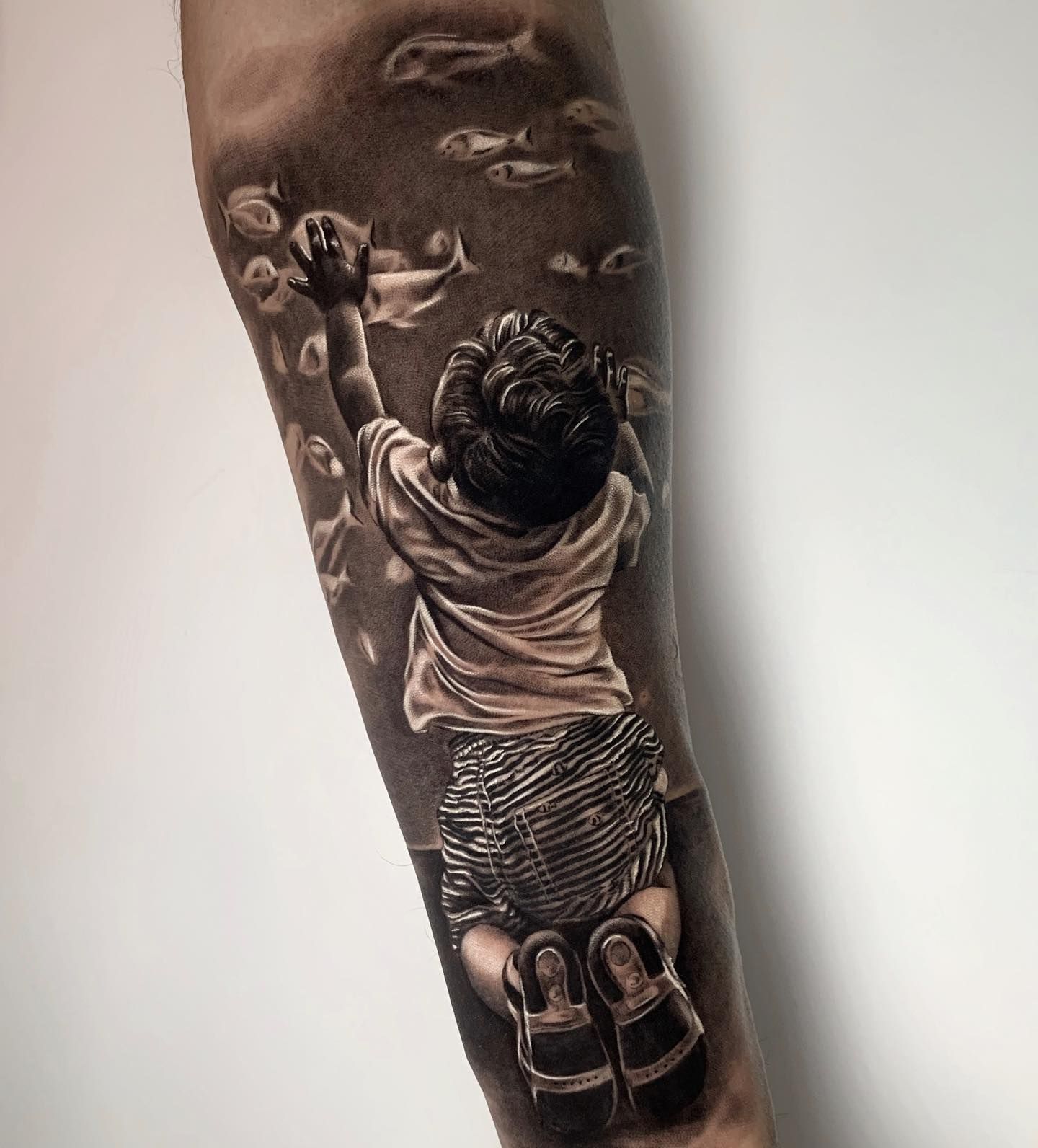 Un tatuaje en blanco y negro de un niño que alcanza el cielo.