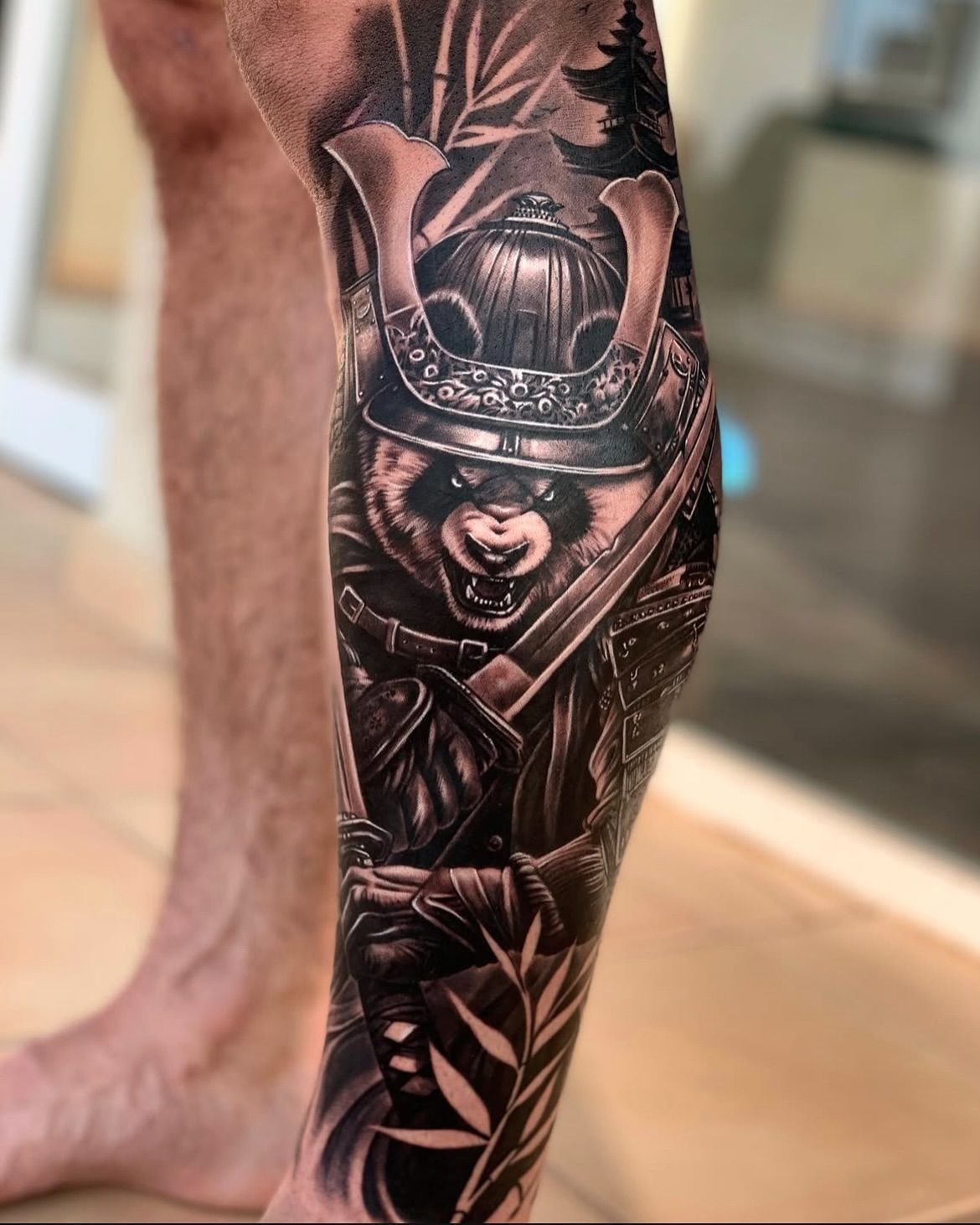 Un tatuaje en blanco y negro de un oso samurái en la pierna de un hombre.