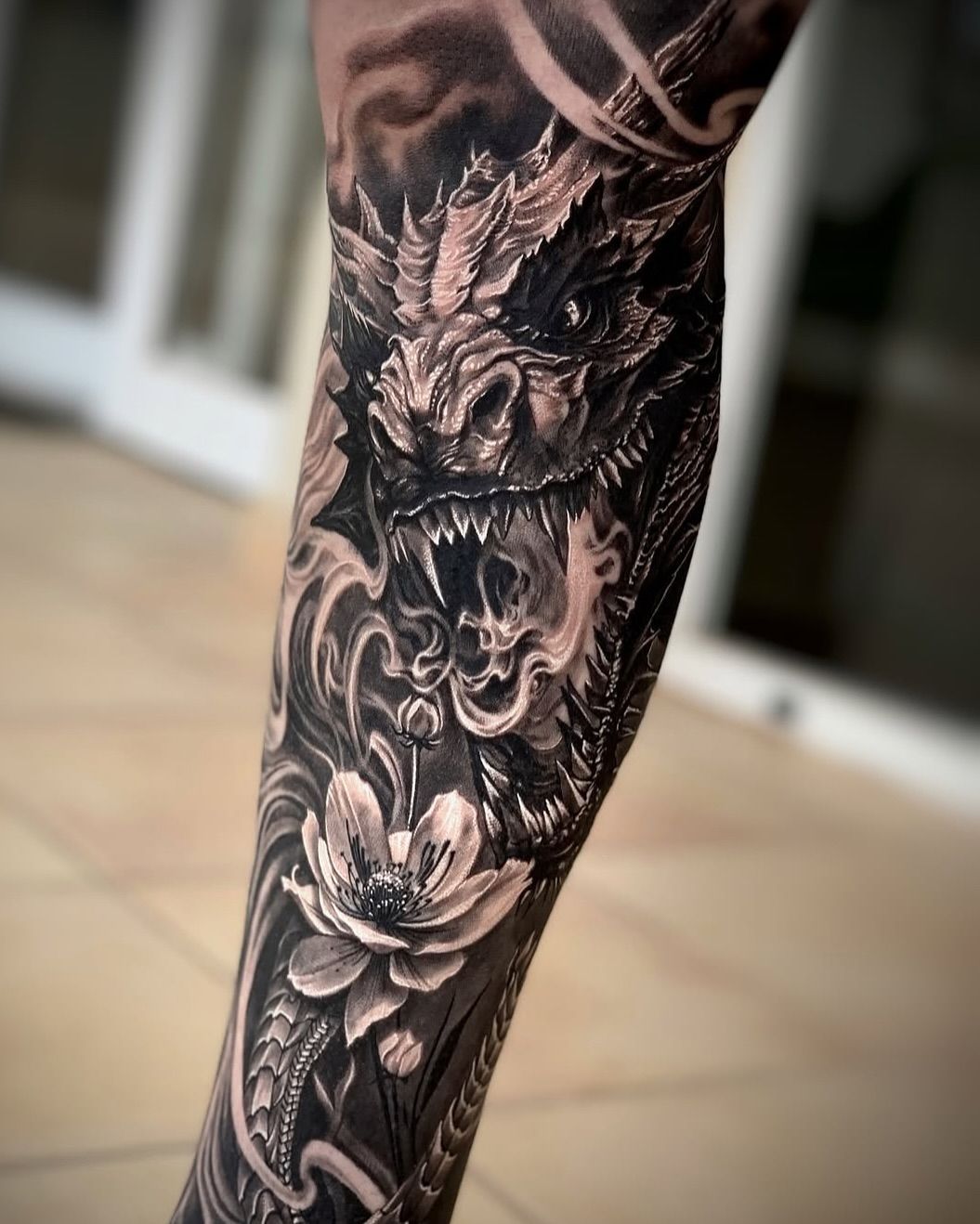 Un tatuaje en blanco y negro de un dragón y flores en una pierna.