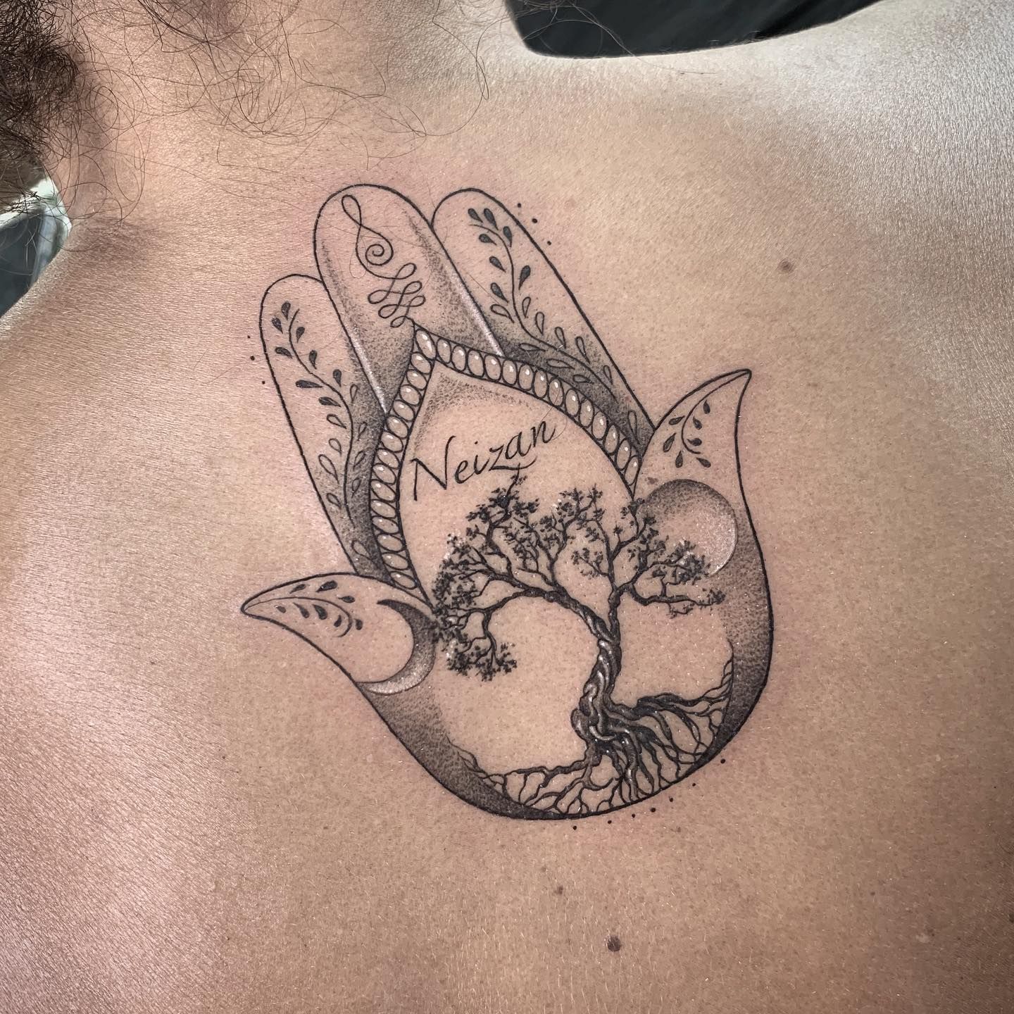 Un tatuaje de una mano hamsa con un árbol dentro de ella en la espalda de un hombre.