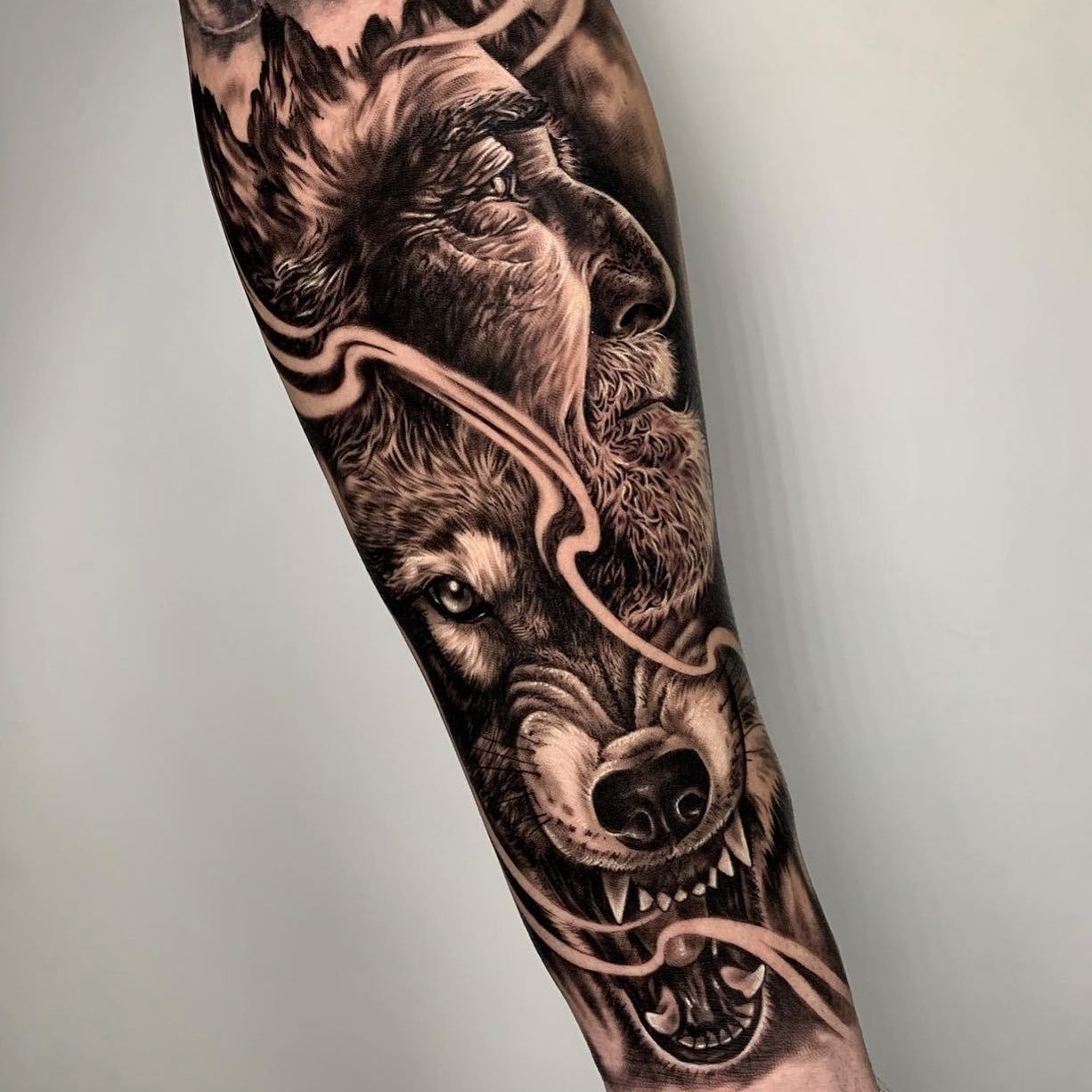 Un tatuaje en blanco y negro de un lobo y un hombre en un antebrazo.