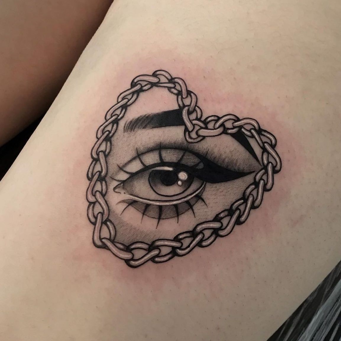 Un tatuaje del ojo de una mujer con una cadena en forma de corazón alrededor.