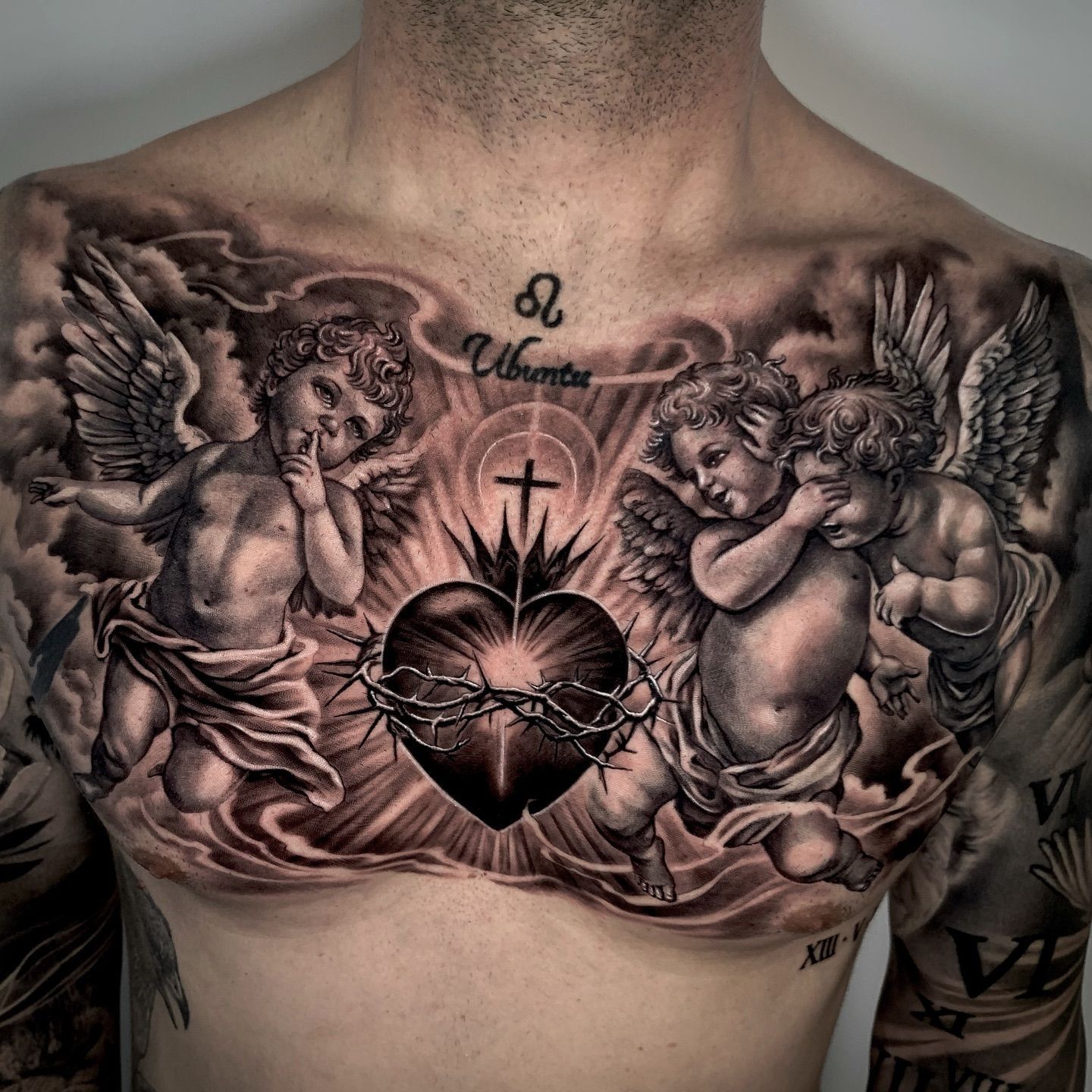 Un hombre tiene un tatuaje de querubines sosteniendo un corazón en su pecho.