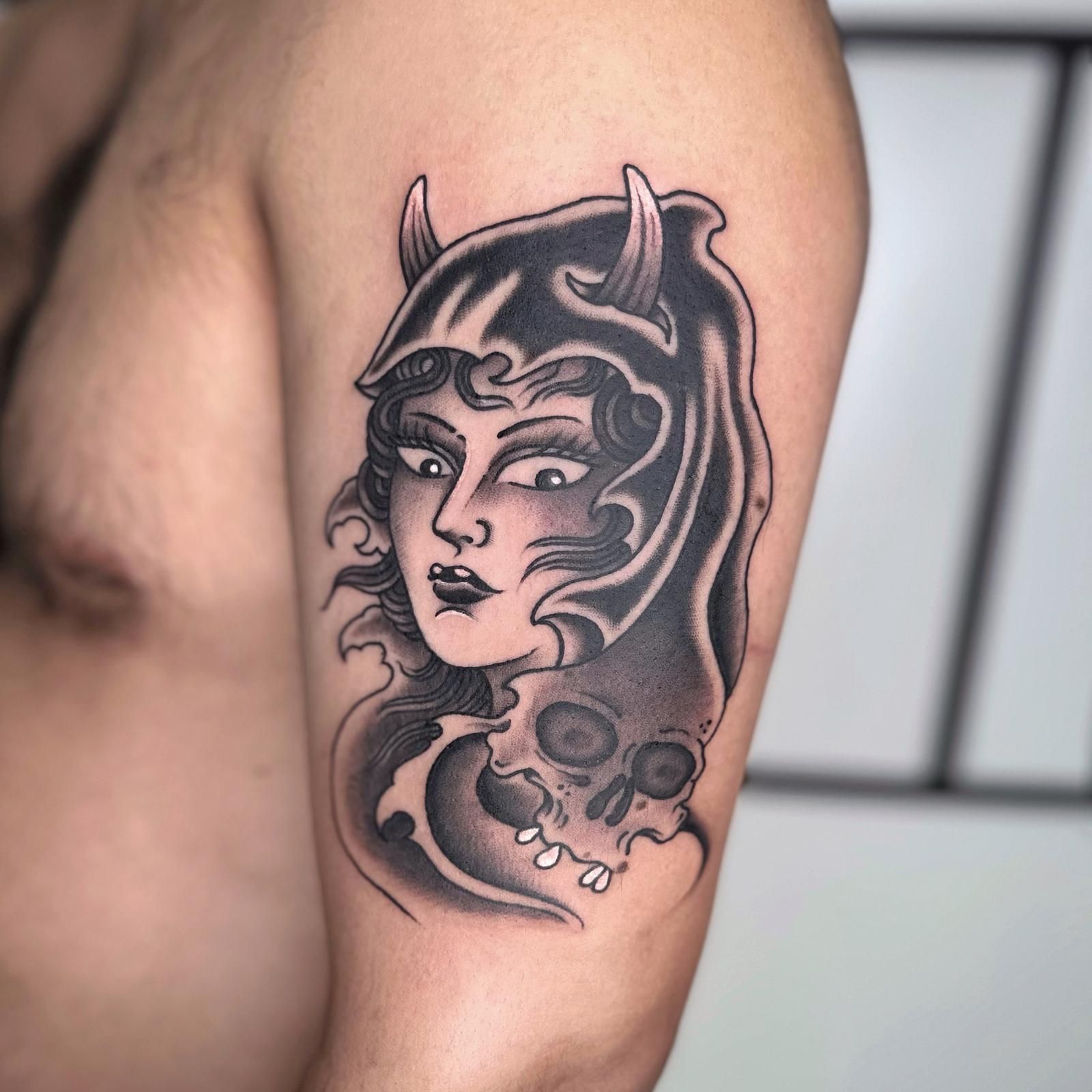 Un hombre tiene un tatuaje de una mujer con cuernos y una calavera en su brazo.