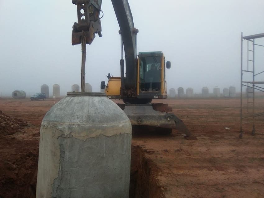 Una excavadora amarilla está cavando un hoyo en un campo de tierra.