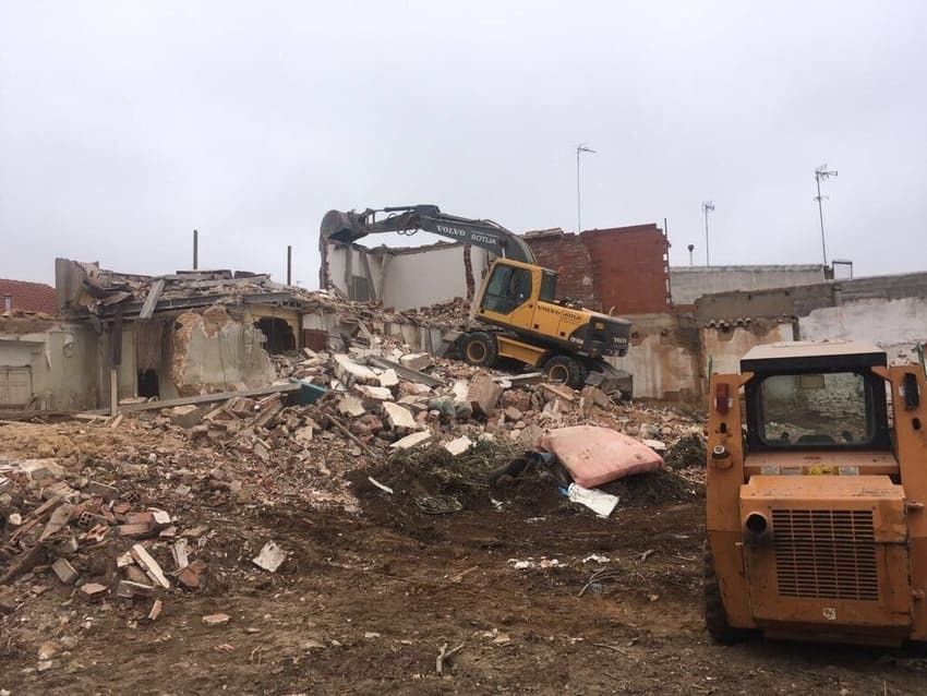 Una excavadora amarilla está demoliendo un edificio al fondo.