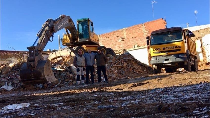 Dos hombres están parados frente a una excavadora y un camión volquete.