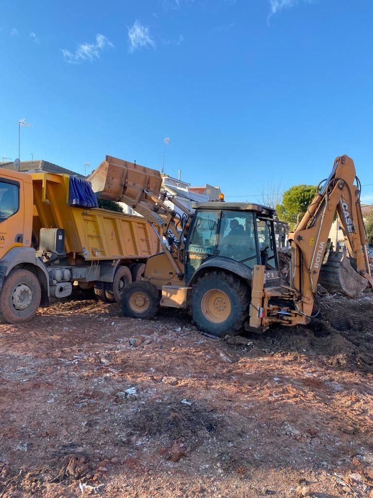 Un camión amarillo con un contenedor de basura adjunto está estacionado en un campo de tierra.