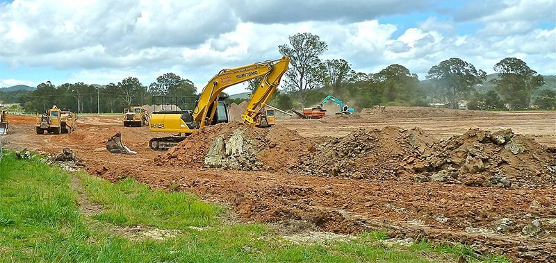 Chantier de construction avec des excavatrices et des engins de terrassement travaillant sur un terrain en terre sous un ciel nuageux.