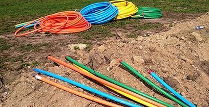 Bobines de conduit coloré (orange, bleu, jaune, vert) et sections coupées sur un monticule de terre.