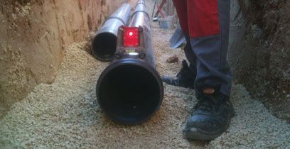 Un ouvrier se trouve à côté de canalisations dans une tranchée ; une canalisation est éclairée en rouge.