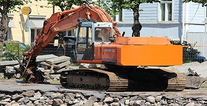 Une pelleteuse orange sur chenilles travaille sur un chantier de construction jonché de débris gris et blancs.