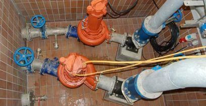 Deux pompes orange avec des vannes bleues et des tuyaux argentés dans une pièce carrelée.