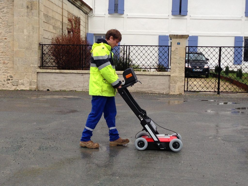 Une personne portant un gilet de sécurité utilise un radar à pénétration de sol sur une chaussée.