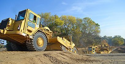 Des engins de chantier jaunes nivellent le sol par une belle journée ensoleillée.
