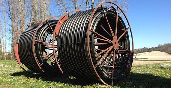 Trois grandes bobines de tuyau ondulé noir sont posées dans un champ herbeux.