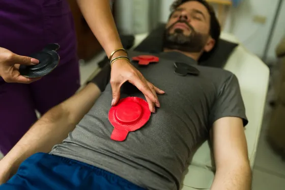 Una persona recibe tratamiento en el pecho; un profesional de la salud le coloca almohadillas rojas en el pecho.