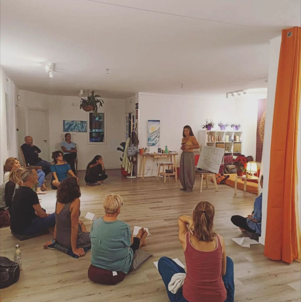 Grupo de personas en una sala bien iluminada, escuchando a una mujer que presenta información.