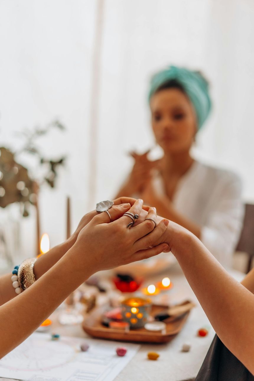 Manos unidas en oración; una mujer con turbante lidera el círculo. Velas encendidas y objetos coloridos sobre la mesa.