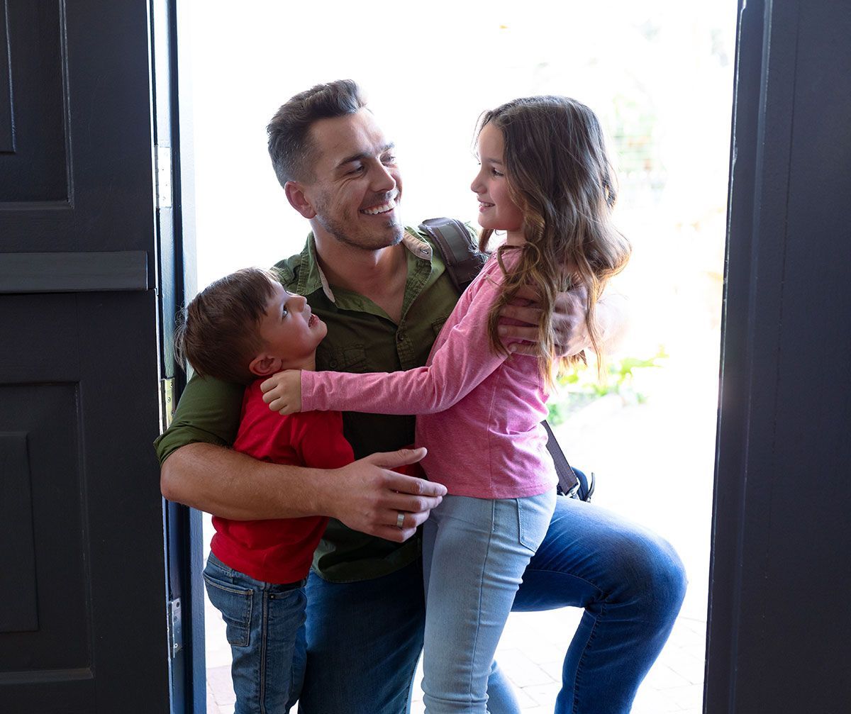 Père qui embrasse ses enfants à l'entrée d'une maison