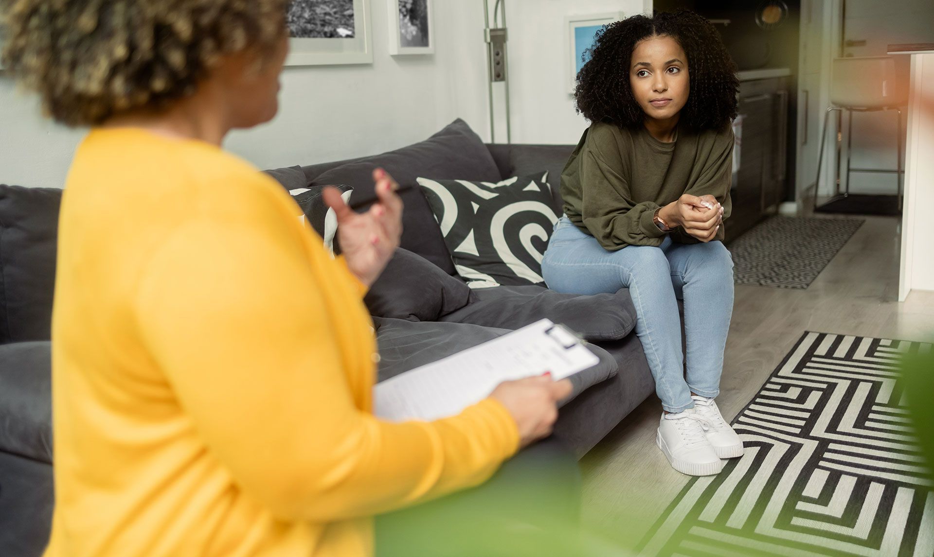 Une femme, assise sur un divan en séance de thérapie, parle à un thérapeute qui tient un bloc-notes.