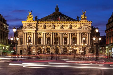 Opéra Garnier, Paris, France au crépuscule ; façade illuminée, lampadaires, phares de voiture flous.