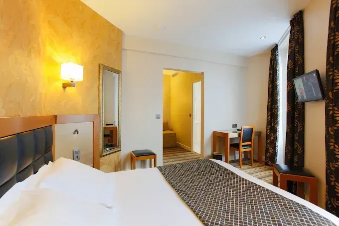 Chambre d'hôtel avec lit, bureau, petite télévision et porte ouverte vers la salle de bain.