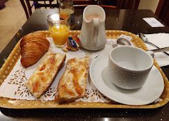 Plateau de petit-déjeuner avec croissant, pain, jus, crème, tasse et ustensiles.