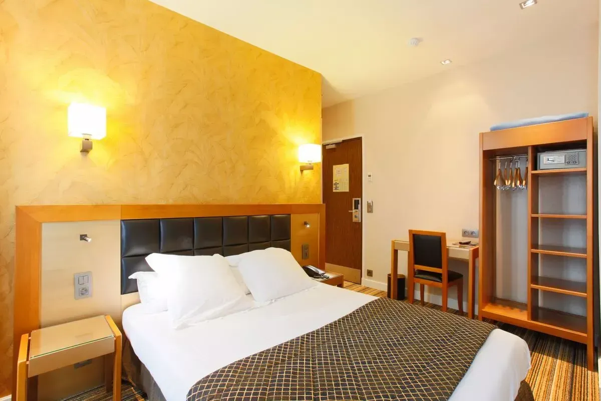 Chambre d'hôtel avec lit, armoire, bureau et lampes. Couleurs beige et marron.