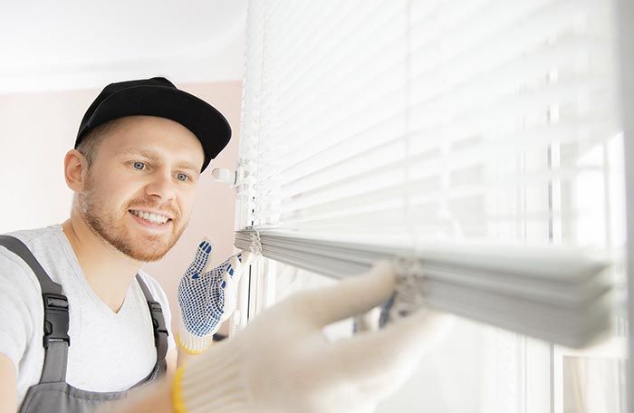 Un hombre está instalando persianas en una ventana.