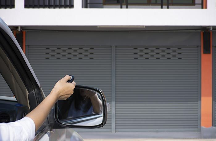 Una persona conduce un automóvil y usa un control remoto para abrir una puerta de garaje.