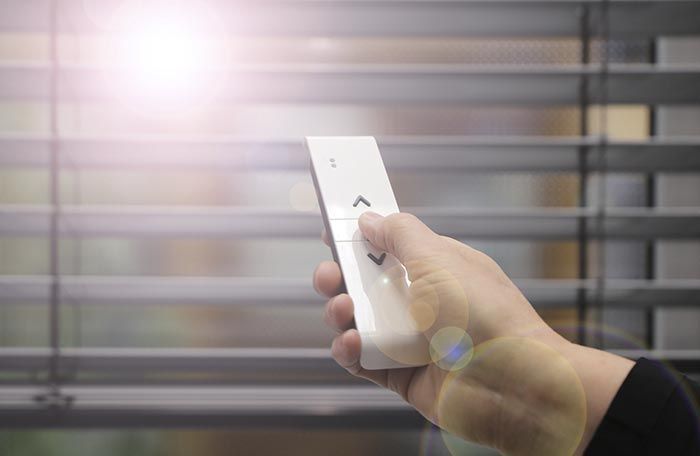 Una persona sostiene un control remoto para controlar las persianas.