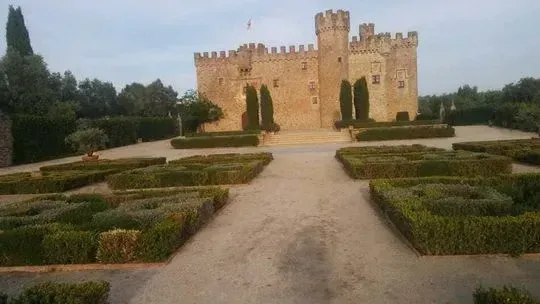 Un gran castillo está rodeado de arbustos y árboles en un parque.
