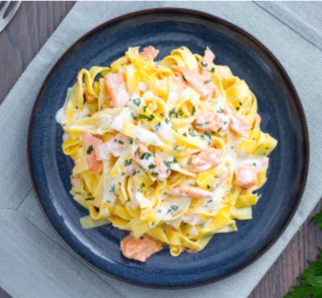 Une assiette bleue garnie de nouilles et de saumon sur une table