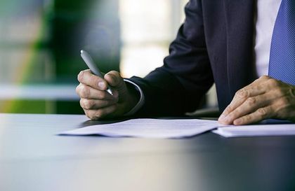 Une personne en costume sombre signe un document avec un stylo à un bureau