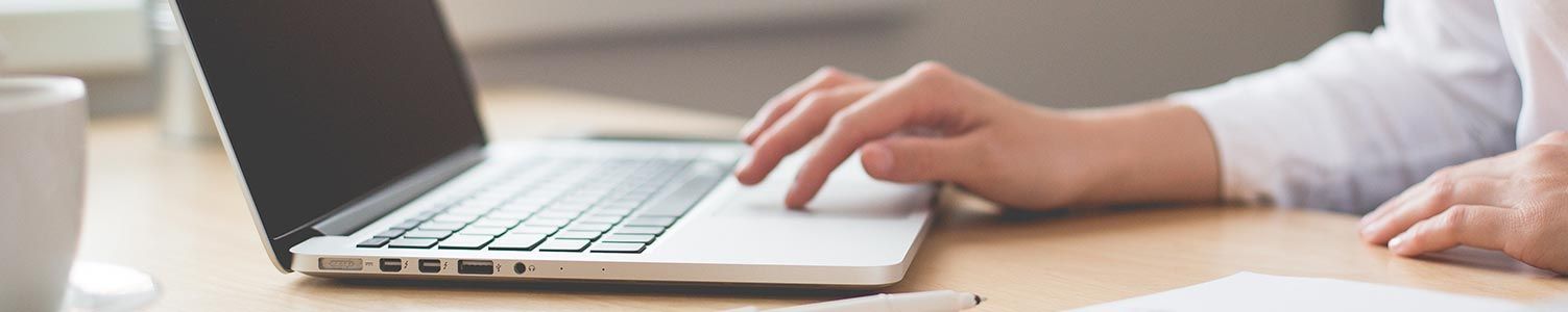 Des mains tapant sur un ordinateur portable argenté posé sur un bureau, avec des tasses de café à proximité