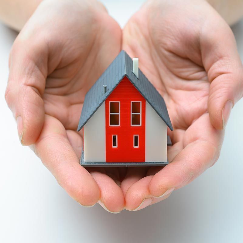 Des mains entourant une petite maquette de maison rouge au toit gris