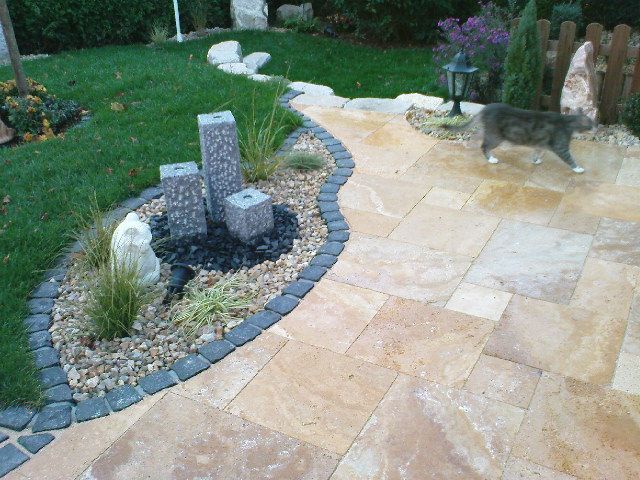 Steinterrasse mit Wasserspiel, Einfassung und einer vorbeilaufenden Katze.