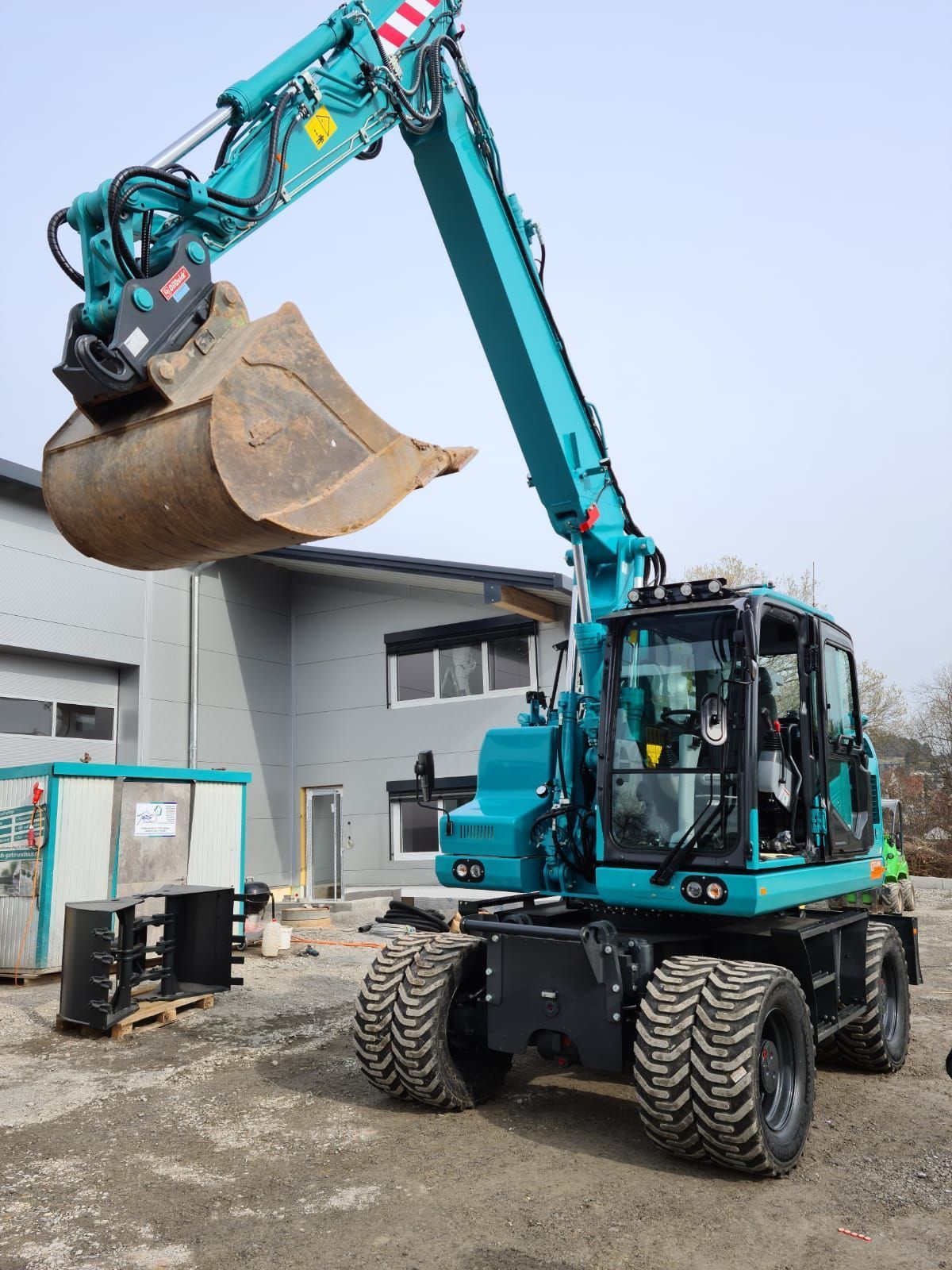 Ein blauer Bagger mit einer großen Schaufel steht vor einem Gebäude