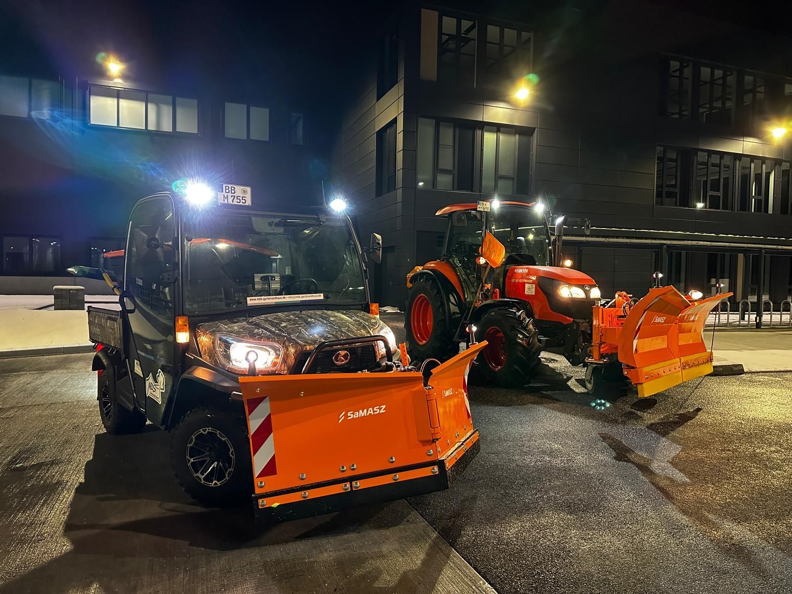 Zwei Schneepflüge stehen nachts vor einem Gebäude.