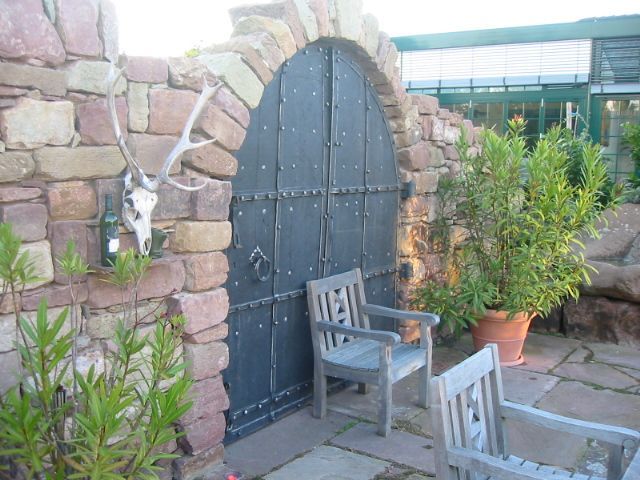 Steinbogen mit schwarzer Metalltür, zwei Holzstühlen und einem Hirschschädel.